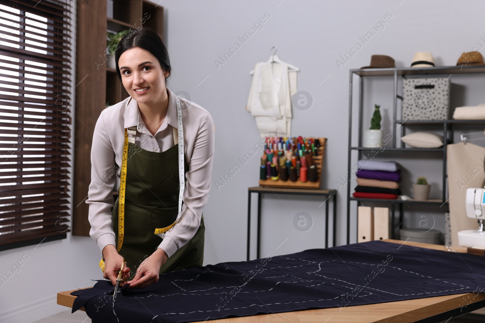 Photo of Dressmaker cutting fabric by following chalked sewing pattern in workshop