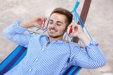 Photo of Young man listening to music in comfortable hammock at seaside