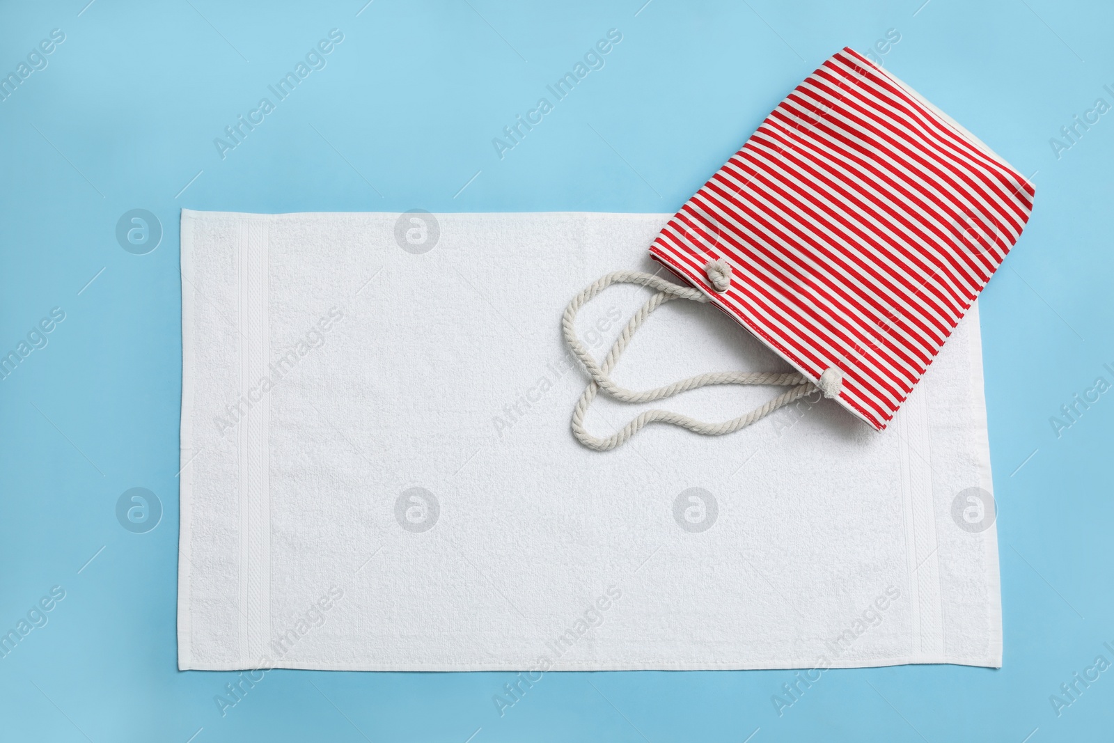 Photo of White towel and beach bag on light blue background, top view