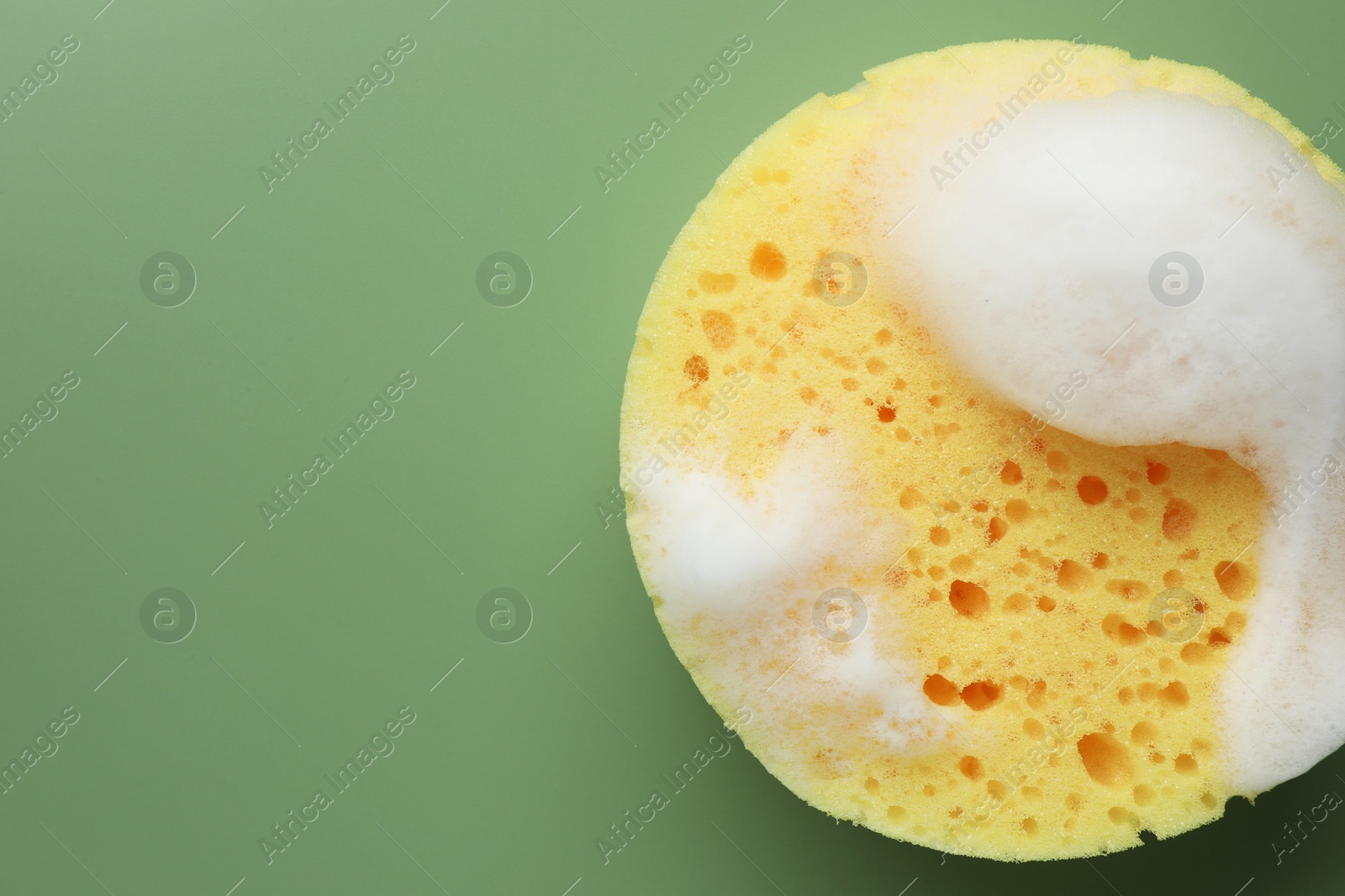 Photo of Yellow sponge with foam on green background, top view. Space for text