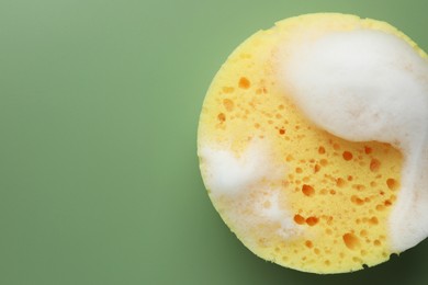 Yellow sponge with foam on green background, top view. Space for text