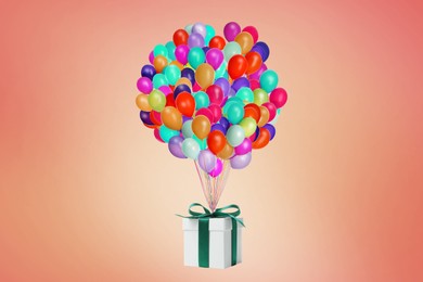 Image of Many balloons tied to gift box on coral background