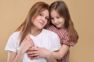 Portrait of mother and her cute daughter on beige background
