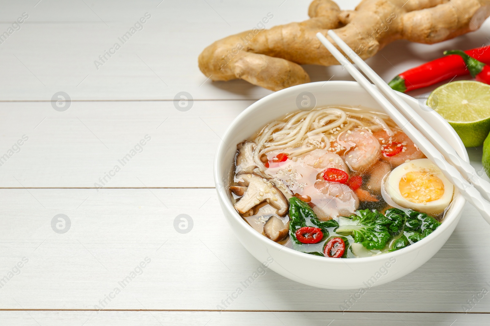 Photo of Tasty ramen with shrimps in bowl and chopsticks on white wooden table. Space for text