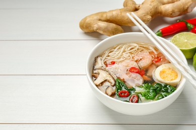 Tasty ramen with shrimps in bowl and chopsticks on white wooden table. Space for text