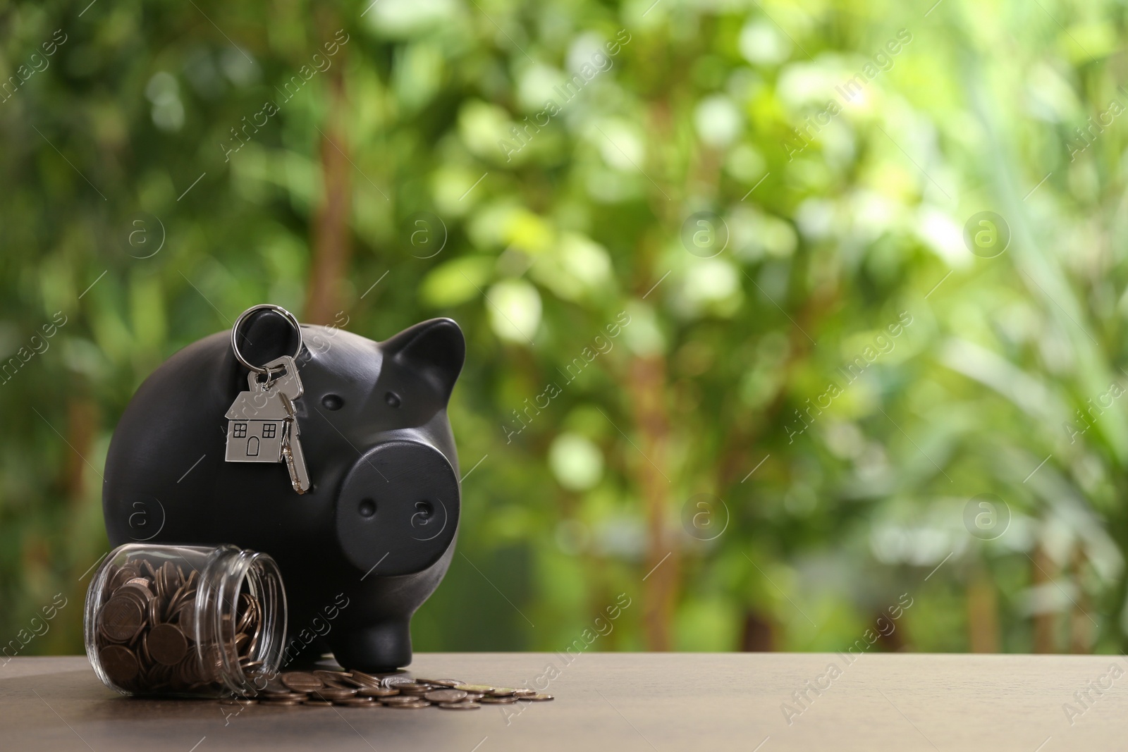 Photo of Piggy bank with key and coins in glass jar on wooden table outdoors, space for text. Saving money concept