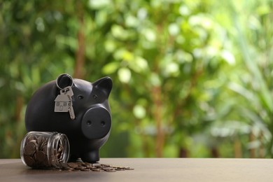 Photo of Piggy bank with key and coins in glass jar on wooden table outdoors, space for text. Saving money concept