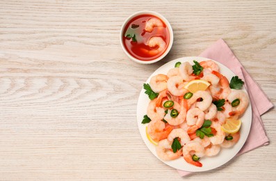 Photo of Tasty boiled shrimps with cocktail sauce, chili, parsley and lemon on light wooden table, flat lay. Space for text