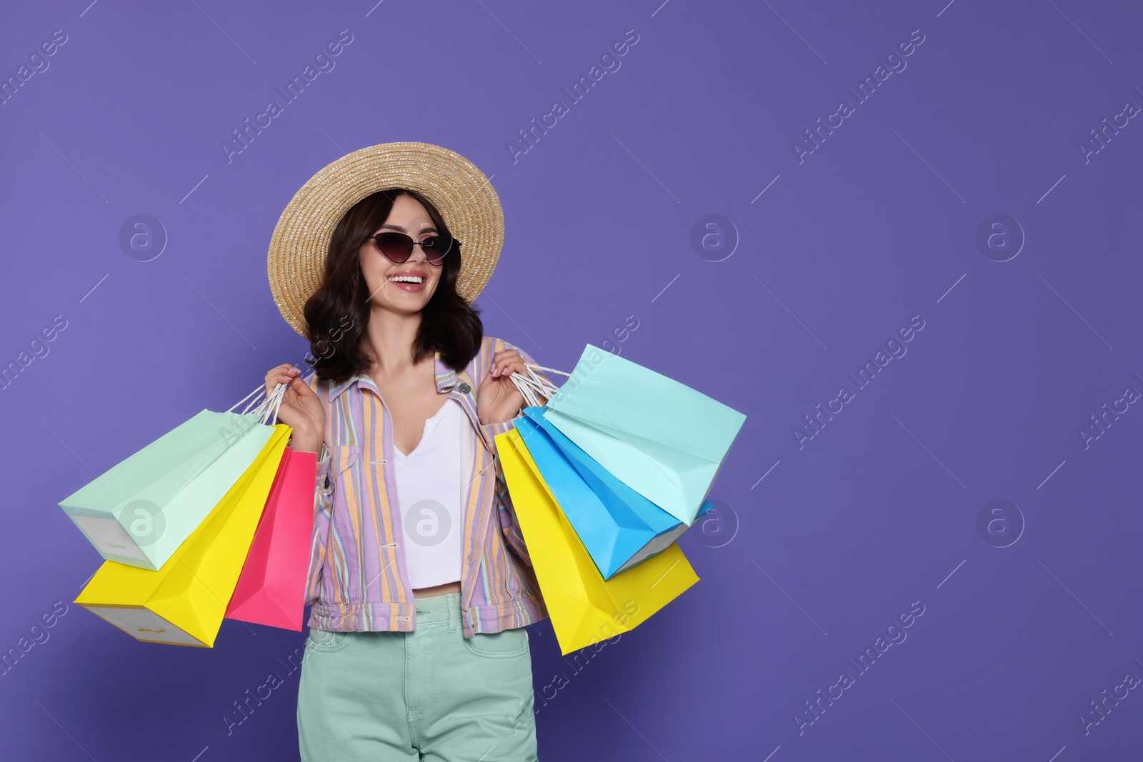 Photo of Beautiful young woman with paper shopping bags on purple background. Space for text