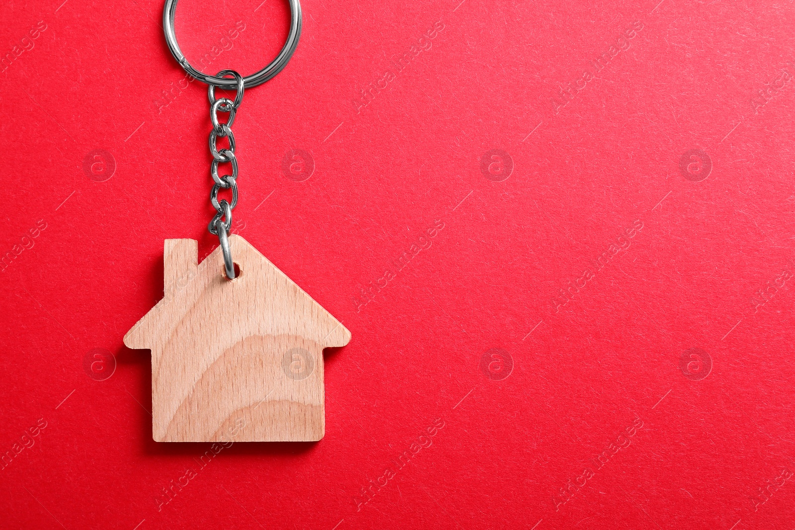 Photo of Wooden keychain in shape of house on red background, top view. Space for text