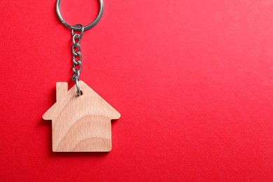 Wooden keychain in shape of house on red background, top view. Space for text