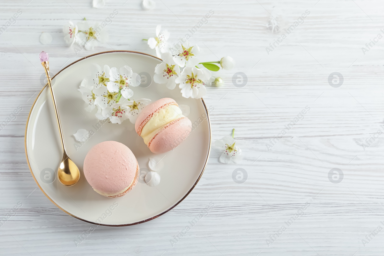 Photo of Delicious pink macarons and flowers on white wooden table, flat lay. Space for text