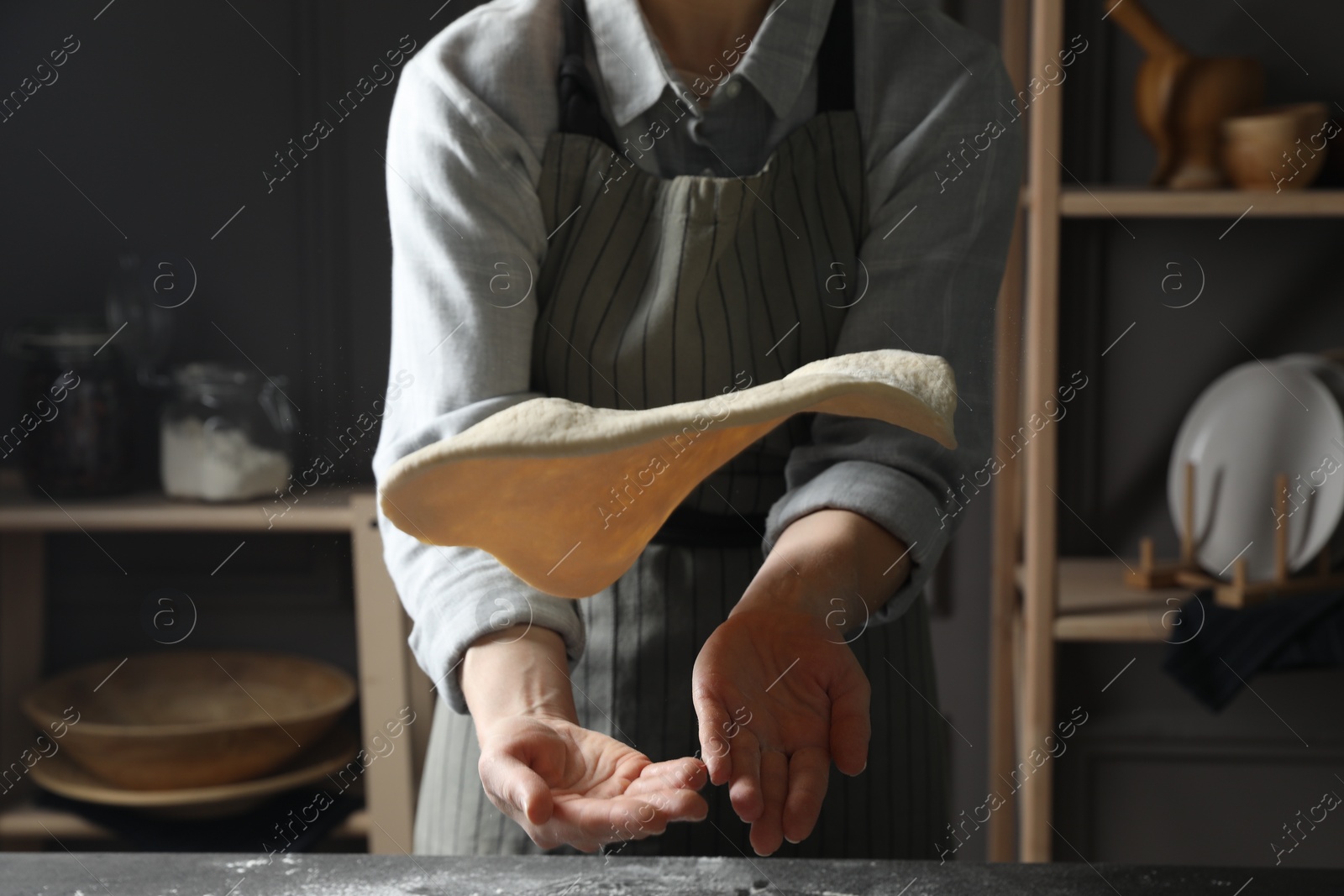 Photo of Woman tossing pizza dough at table in kitchen, closeup