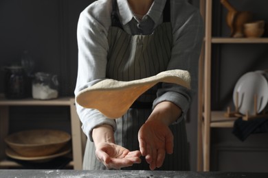 Woman tossing pizza dough at table in kitchen, closeup