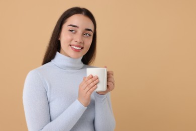 Photo of Happy young woman holding white ceramic mug on beige background, space for text