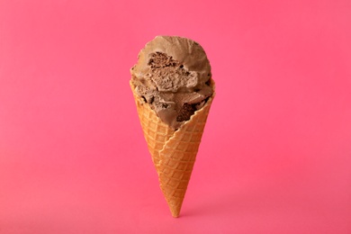 Photo of Delicious chocolate ice cream in waffle cone on pink background
