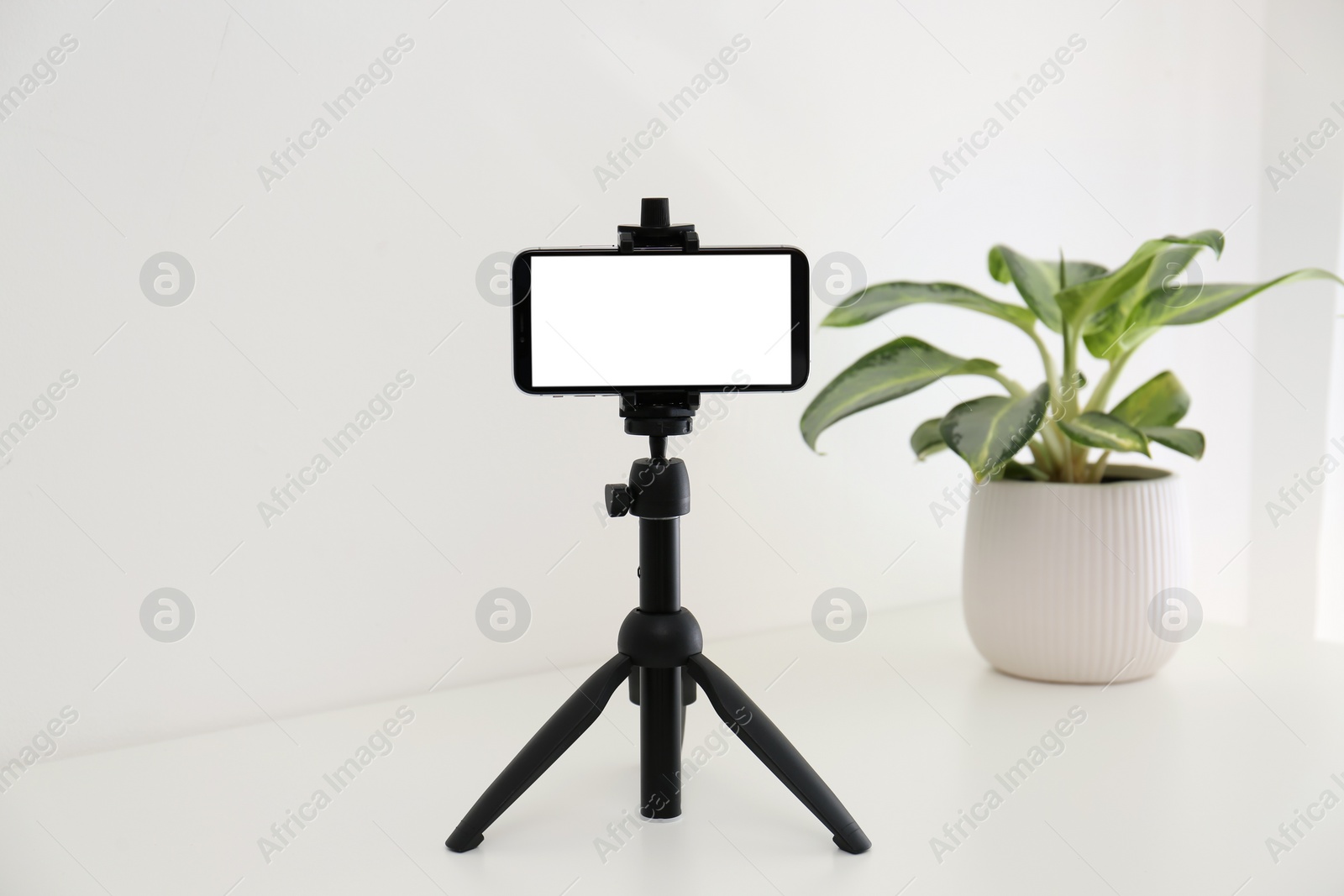 Photo of Smartphone with blank screen fixed to tripod on white table indoors. Mockup for design