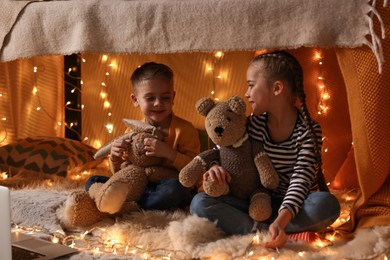 Kids with toys playing in decorated play tent at home