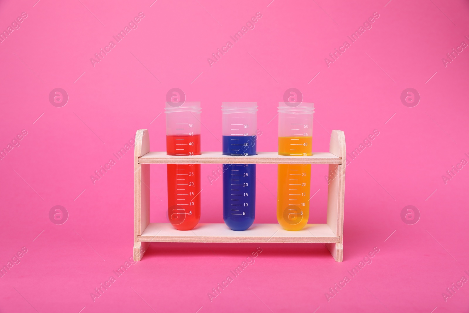 Photo of Test tubes with colorful liquids in wooden stand on bright pink background. Kids chemical experiment set