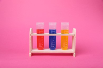 Photo of Test tubes with colorful liquids in wooden stand on bright pink background. Kids chemical experiment set