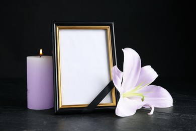 Funeral photo frame with ribbon, violet lily and candle on dark table against black background