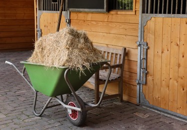 Photo of Wheelbarrow with hay near wooden stable outdoors