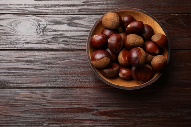 Photo of Sweet fresh edible chestnuts in bowl on wooden table, top view. Space for text