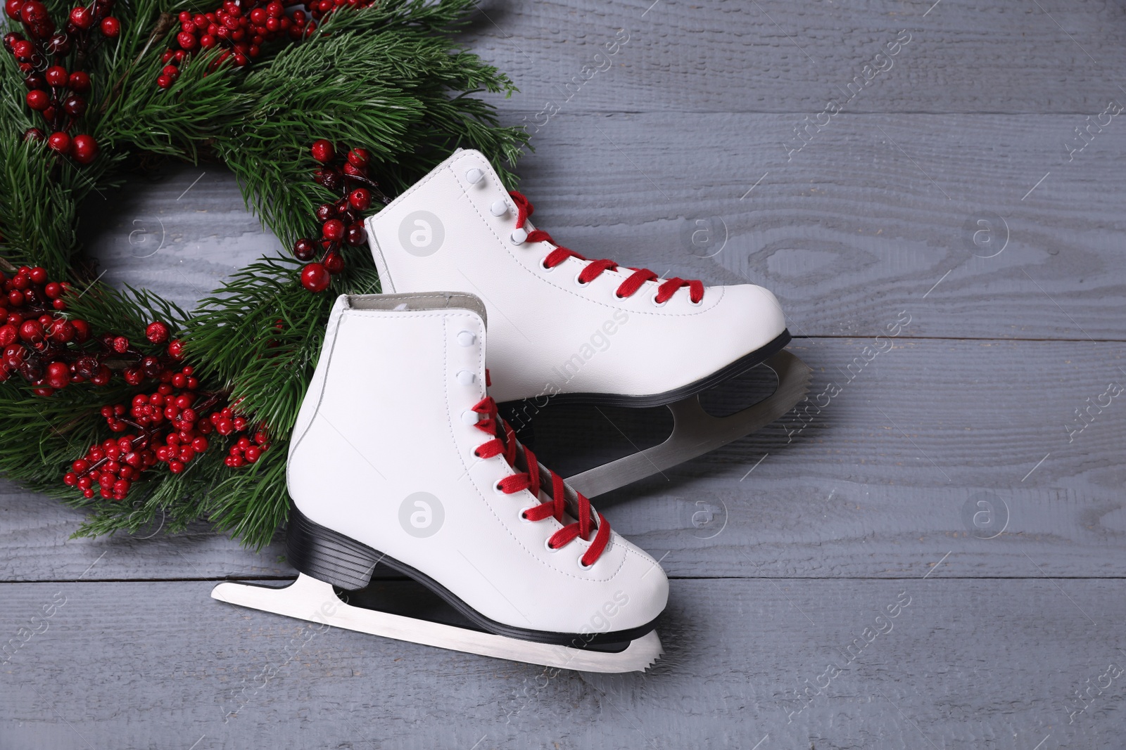 Photo of Pair of ice skates and Christmas wreath on grey wooden background, flat lay