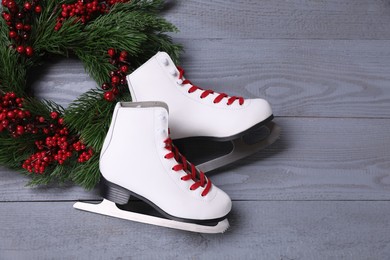 Photo of Pair of ice skates and Christmas wreath on grey wooden background, flat lay