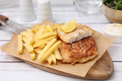 Photo of Tasty soda water battered fish, potato chips and lemon slice on white wooden table