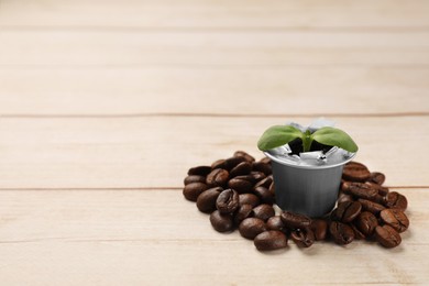 Photo of Green seedling growing in coffee capsule and beans on wooden table, space for text