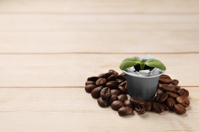 Green seedling growing in coffee capsule and beans on wooden table, space for text