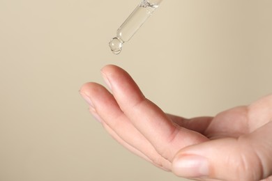 Photo of Woman applying cosmetic serum onto finger on beige background, closeup