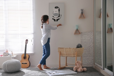 Photo of Decorator hanging picture on white wall in baby room. Interior design