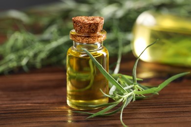Photo of Bottle of essential oil and fresh tarragon leaves on wooden table, closeup