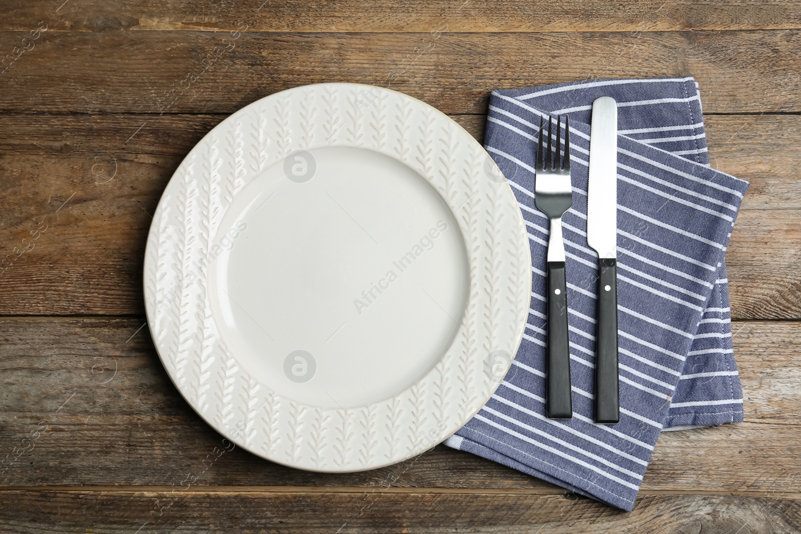 Photo of Empty ornate plate with cutlery and napkin on wooden table, flat lay