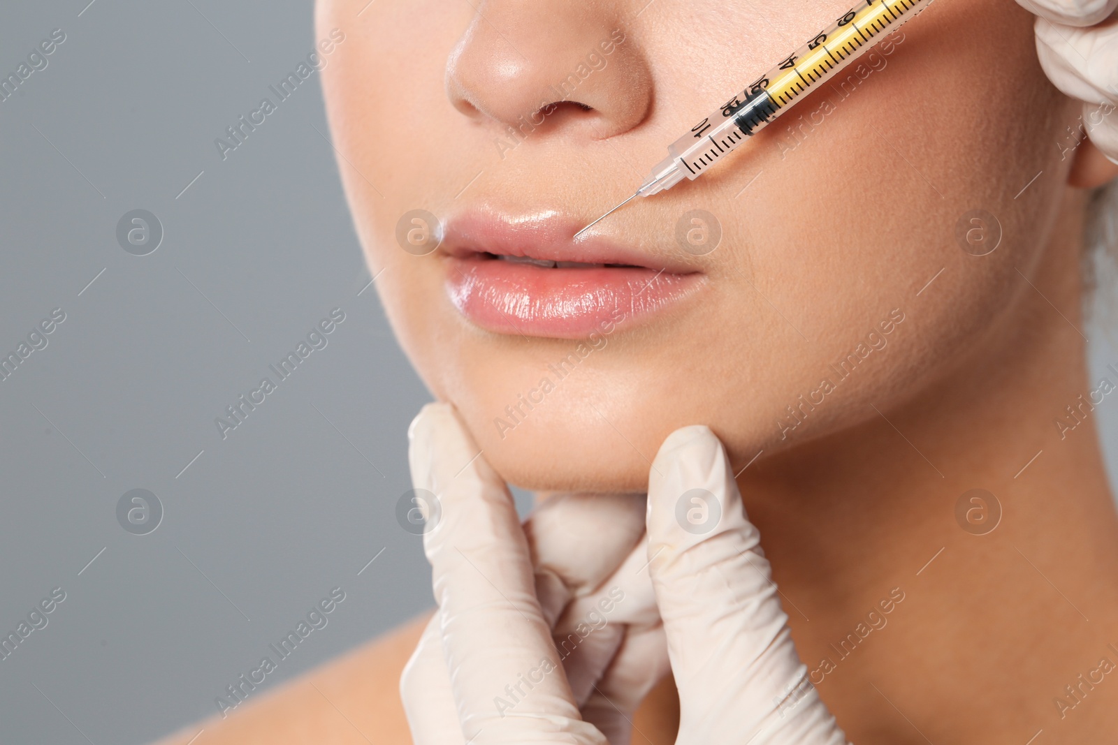 Photo of Young woman getting lips injection on grey background, closeup. Cosmetic surgery