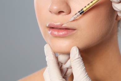 Young woman getting lips injection on grey background, closeup. Cosmetic surgery