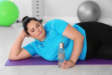 Overweight woman lying on mat in gym