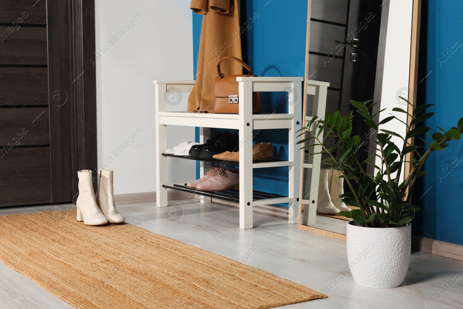 Photo of Stylish hallway with shoe storage bench and mirror near blue wall. Interior design