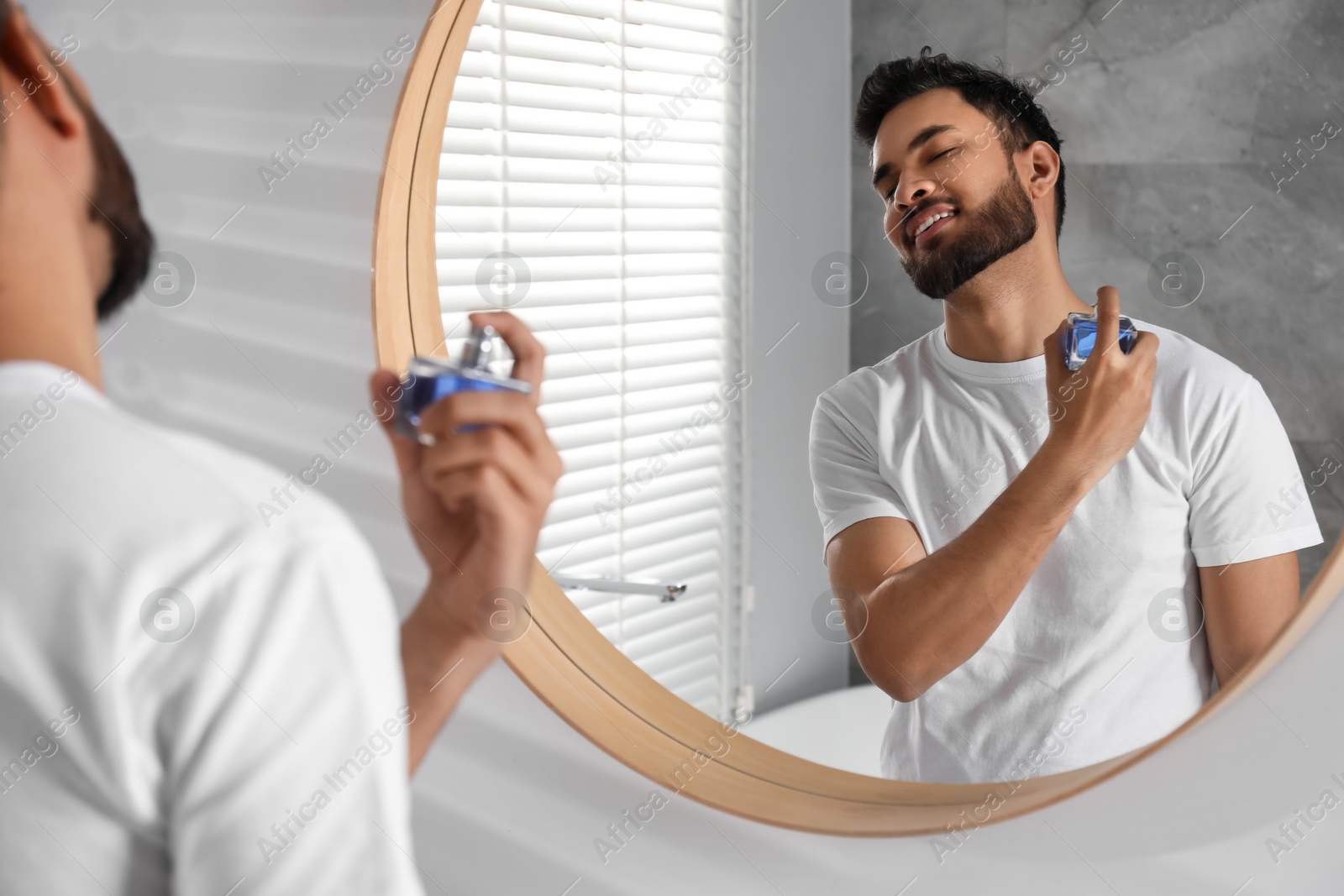 Photo of Man spraying luxury perfume near mirror indoors