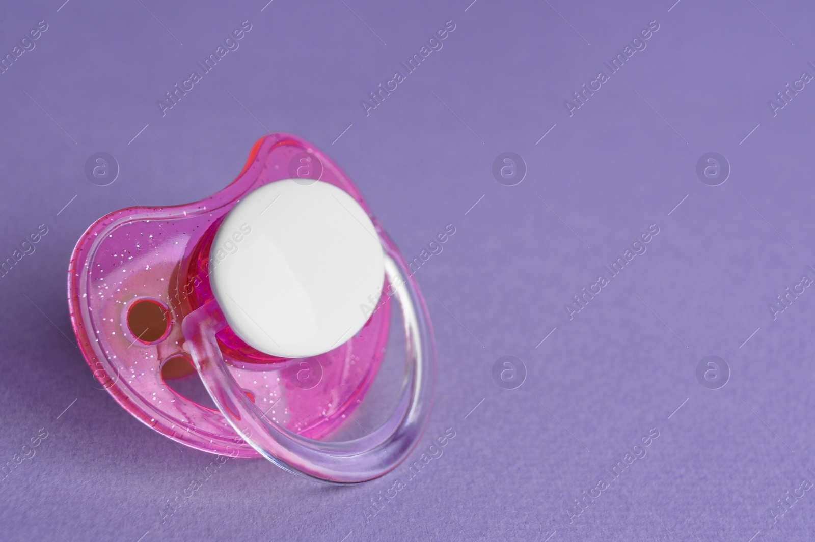 Photo of One new baby pacifier on purple background, closeup. Space for text