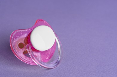 Photo of One new baby pacifier on purple background, closeup. Space for text