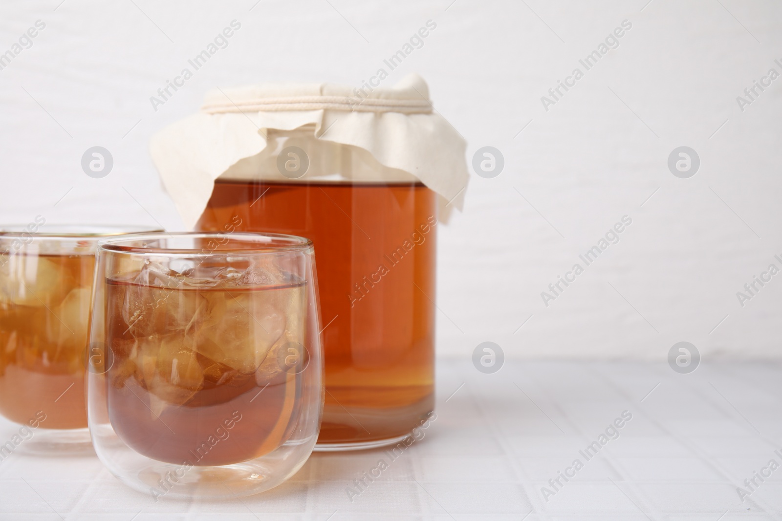 Photo of Tasty kombucha with ice cubes on white tiled table, space for text