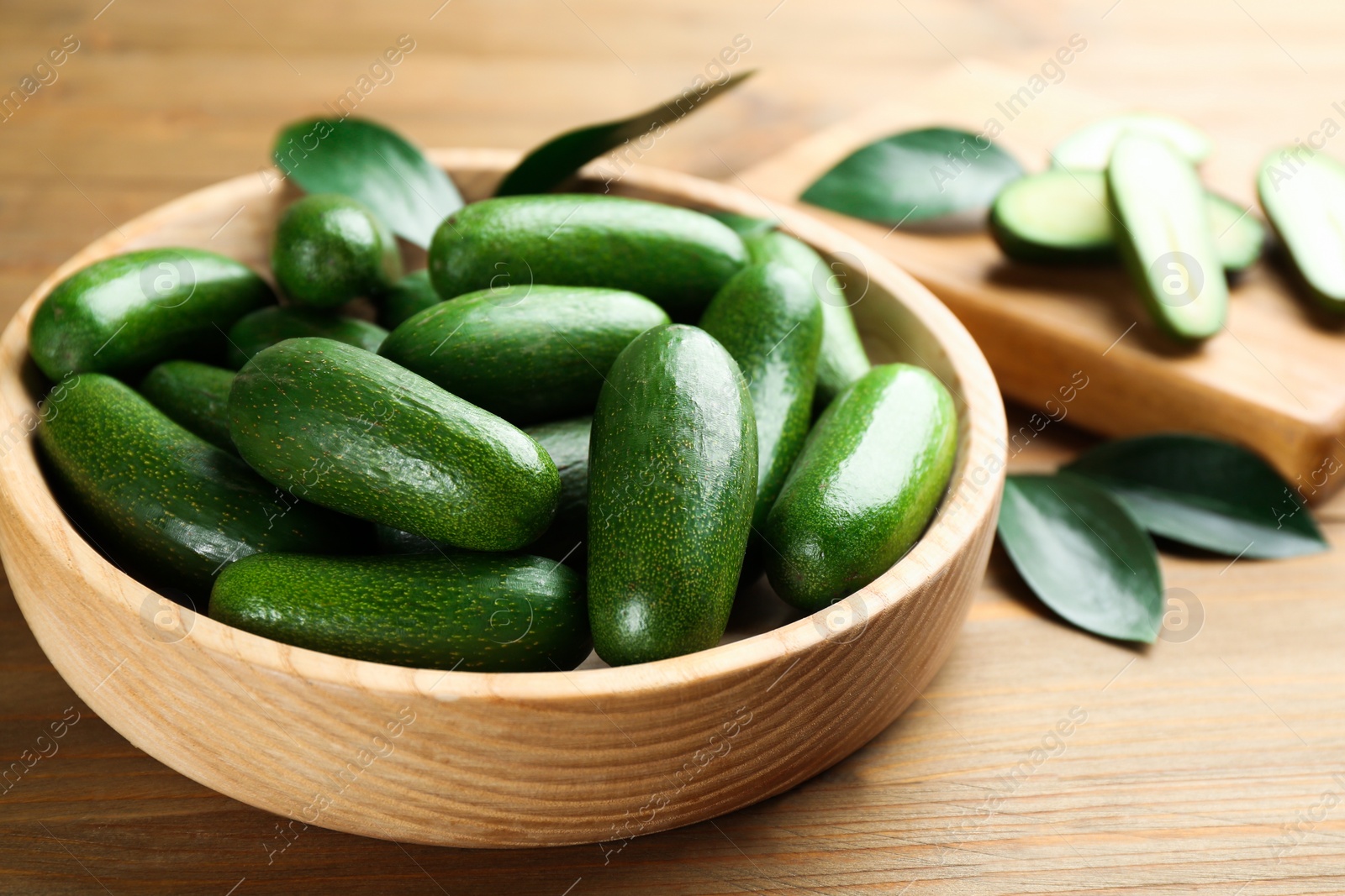 Photo of Fresh seedless avocados with green leaves in bowl on wooden table, closeup