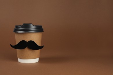 Photo of Paper cup of drink with fake mustache on brown background, space for text