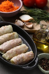 Photo of Uncooked stuffed cabbage rolls and ingredients on grey table