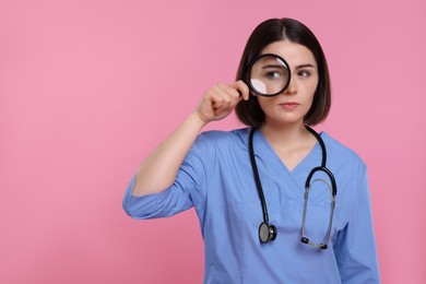 Photo of Doctor with stethoscope looking through magnifier on pink background, space for text