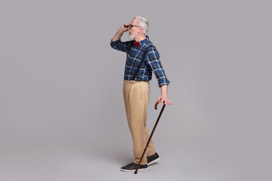 Senior man with walking cane on gray background