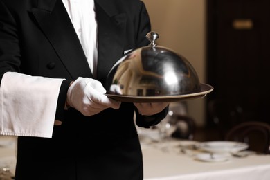 Photo of Butler holding metal tray with lid in restaurant, closeup
